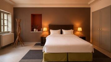 Una habitación de hotel con una cama grande, dos mesitas de noche con lámparas, un radiador, una lámpara de pie de madera y un armario.