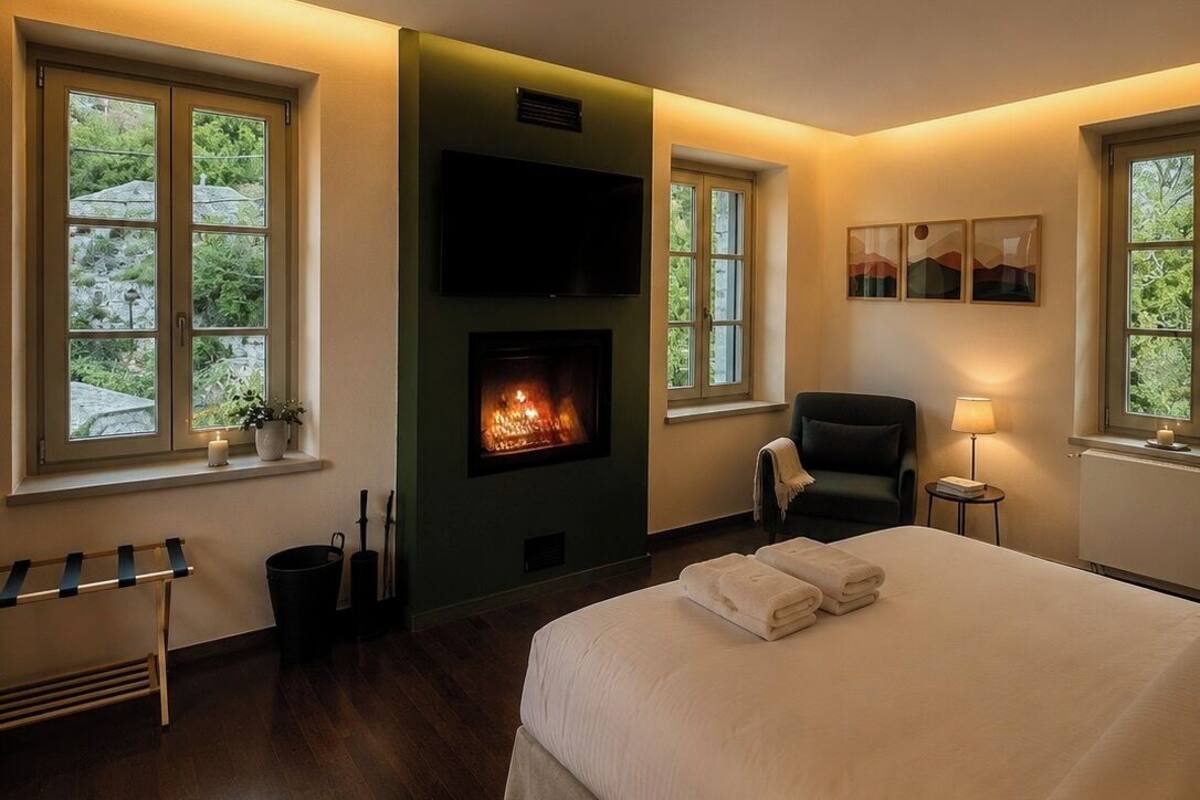 Una habitación de hotel con cama, chimenea, televisión y ventanas amplias.