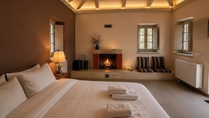 A bedroom with a fireplace, a bed with pillows, a nightstand with a lamp, and a window. - Monopatia Resort (Zagori)