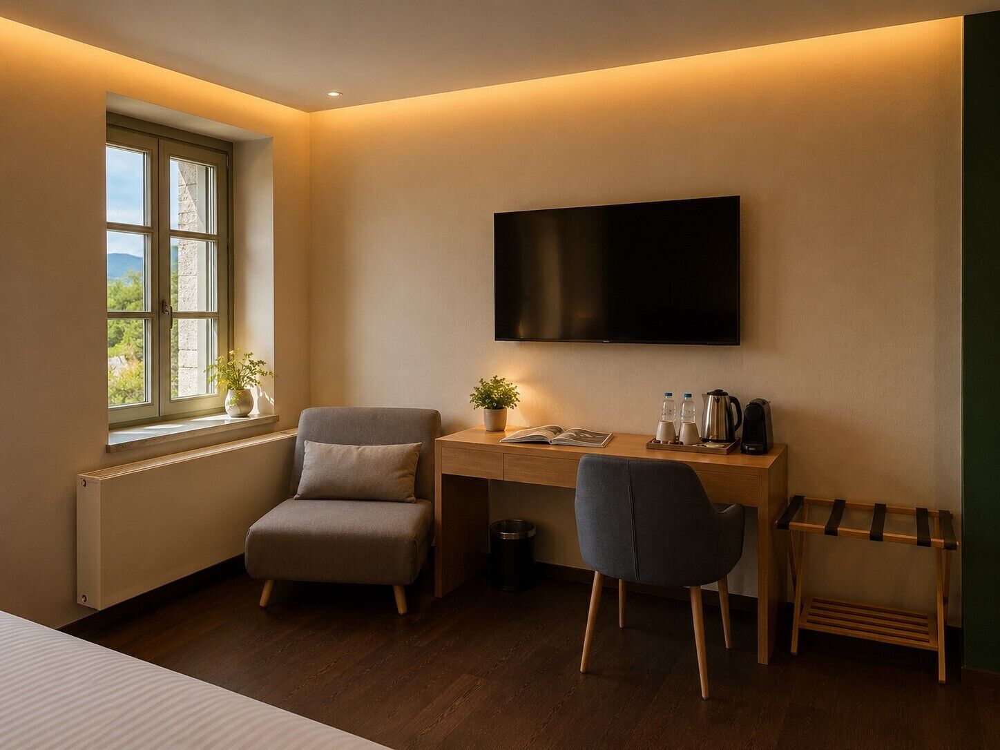 A hotel room with a desk, two chairs, a TV, a radiator, a window with plants, and a view of greenery.