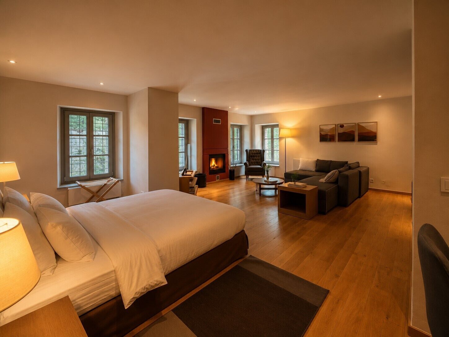 Une chambre spacieuse avec un grand lit, un coin salon avec un canapé et des fauteuils, une cheminée et de nombreuses fenêtres.