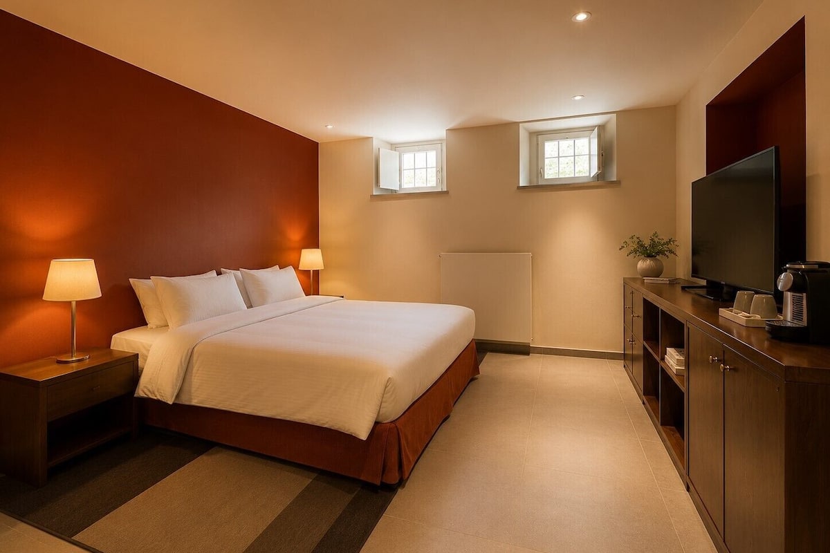Una habitación de hotel con cama, lámparas de noche, televisor, cafetera y radiador.