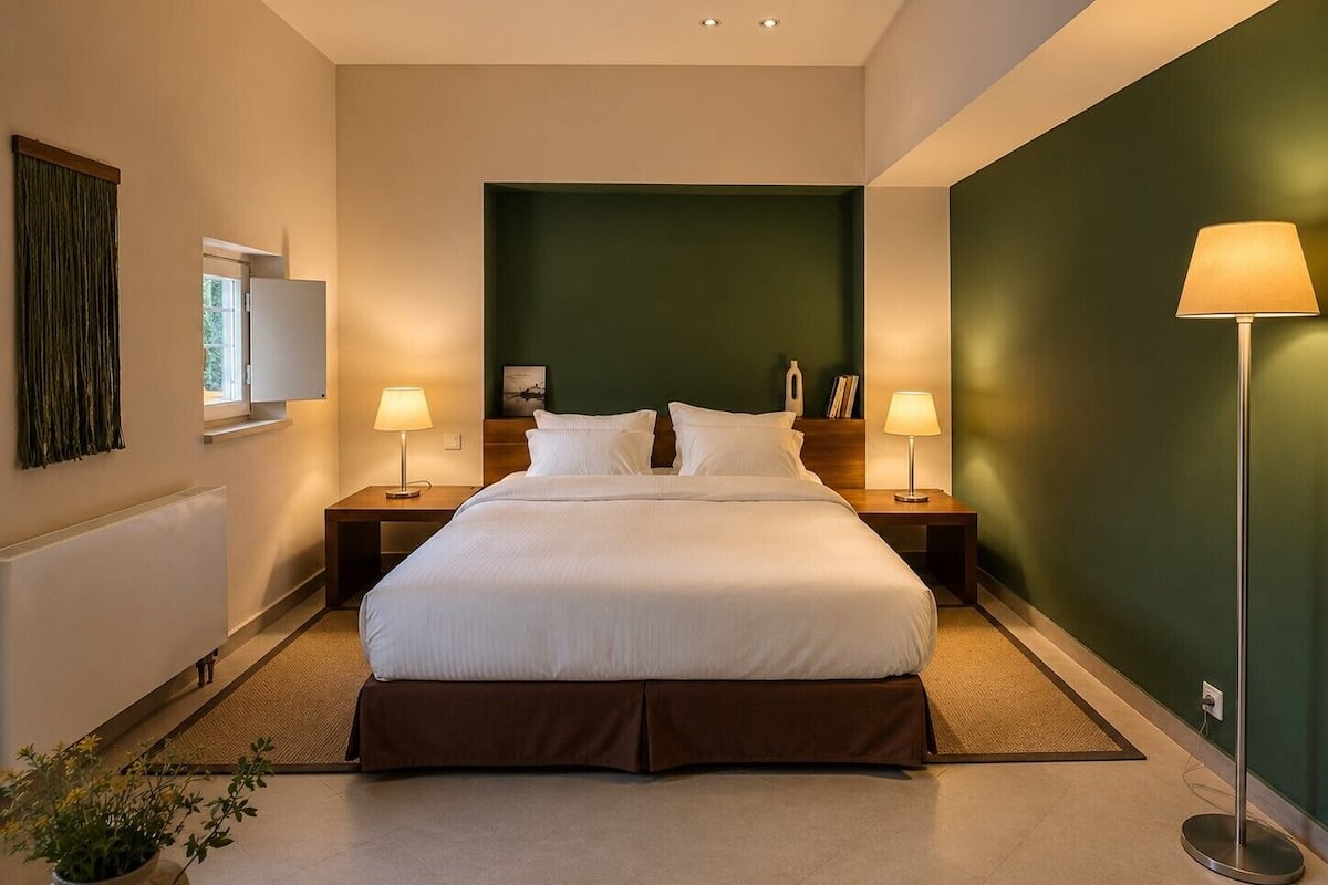Una habitación de hotel con una cama grande, dos mesitas de noche, una lámpara de pie, una ventana con cortinas y una pared verde decorativa.