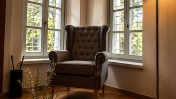 Una habitación de esquina con un sillón capitoné, una lámpara de pie, un libro y una vela sobre una mesa.