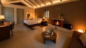 A hotel room with a bed, bedside tables, a fireplace, a round coffee table, and a desk with a chair. - Monopatia Resort (Zagori)