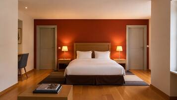 Een hotelkamer met een groot bed, twee nachtkastjes met lampen, een stoel, een tafeltje met een boek en een houten vloer.