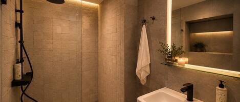 Un baño moderno con ducha de vidrio, lavamanos blanco y espejo con repisa superior.