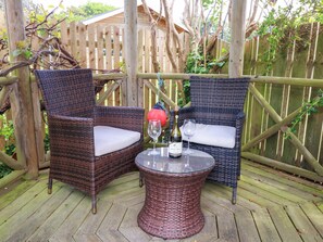 An outdoor seating area with wicker chairs and a glass table, surrounded by a wooden deck and a wooden fence. - Little Gem (Weymouth)
