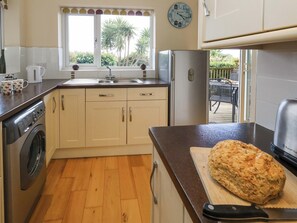 A kitchen with a washing machine, a large bread loaf on a cutting board, and a clock on the wall. - Little Gem (Weymouth)