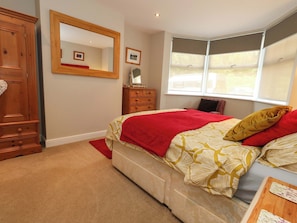 A bedroom with a bed, a dresser, a mirror, a window, and a door. - Little Gem (Weymouth)