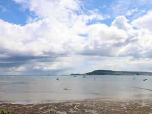 A coastal scene with calm waters, boats, and a distant hill. - Little Gem (Weymouth)