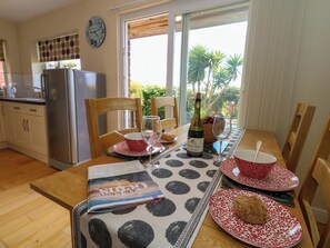 A dining table set with plates, a wine bottle, and a magazine. - Little Gem (Weymouth)