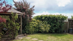 Un giardino con una pergola in legno, un siepe e un sentiero in pietra.