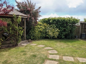A garden with a wooden pergola, a hedge, and a stone pathway. - Little Gem (Weymouth)