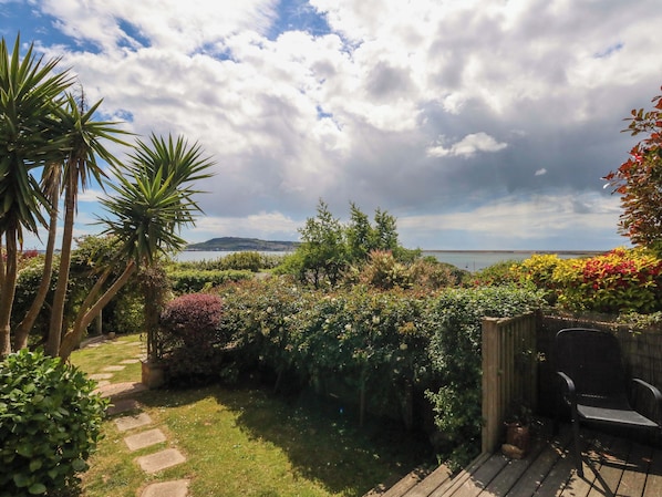 A garden with a variety of plants, a wooden deck, and a view of the sea. - Little Gem (Weymouth)