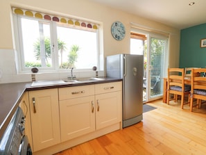 A kitchen with a refrigerator, a sink, and a window with a view of palm trees. - Little Gem (Weymouth)