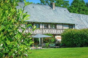 A Tudor-style house with a steeply pitched roof, a visible chimney, and a garden with a patio area. - Authentic house with pond near Étretat (Yebleron)