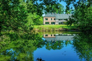 Ein Haus mit einem großen Teich davor, umgeben von üppigem Grün.