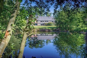 Ein traditionelles Gebäude mit einer symmetrischen Fassade, ein Teich im Vordergrund, der das Gebäude widerspiegelt, und ein gepflegter Rasen.