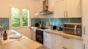 Una cocina moderna con armarios blancos, una campana extractora de acero inoxidable, un lavamanos doble y una ventana con vistas a la vegetación.