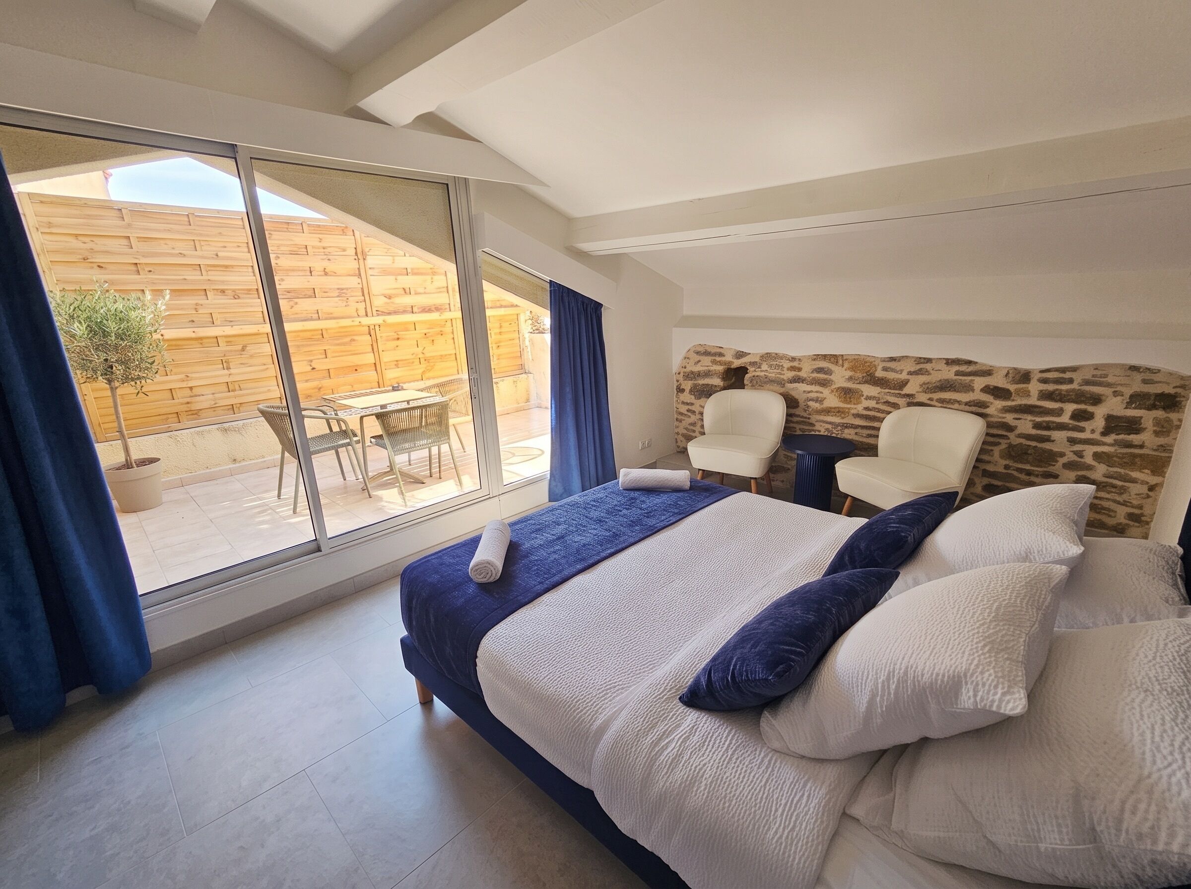 Une chambre avec un grand lit, un mur en pierre et une vue sur une terrasse extérieure.