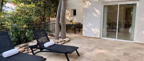 A patio with two lounge chairs, a table with breakfast items, and a building with a glass door.