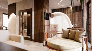 A modern interior with a sofa, a round bed with pillows, a kitchen area, and a dining table with a wine glass.