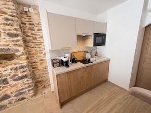 A compact kitchen with a stone wall, wooden cabinets, a built-in microwave, and a coffee maker. - Villa Onyra (Saint-Cyr-sur-Mer)