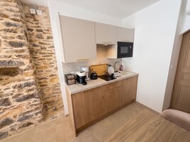 A compact kitchen with a stone wall, wooden cabinets, a built-in microwave, and a coffee maker.