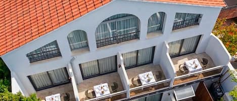 A multi-story building with a red-tiled roof, balconies with tables and chairs, and a well-maintained garden area.