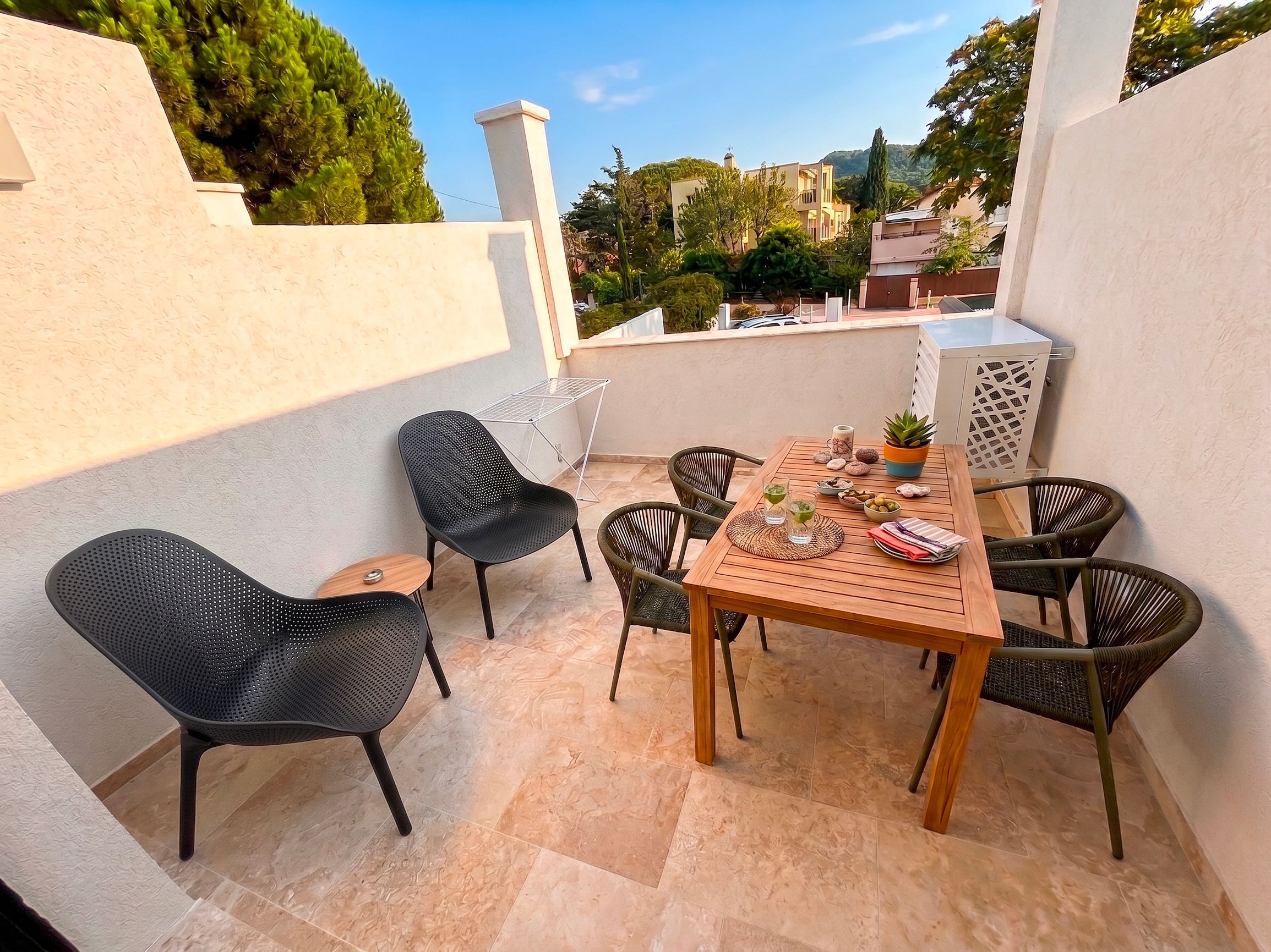 An outdoor patio with a wooden table and chairs, a drying rack, and a potted plant.