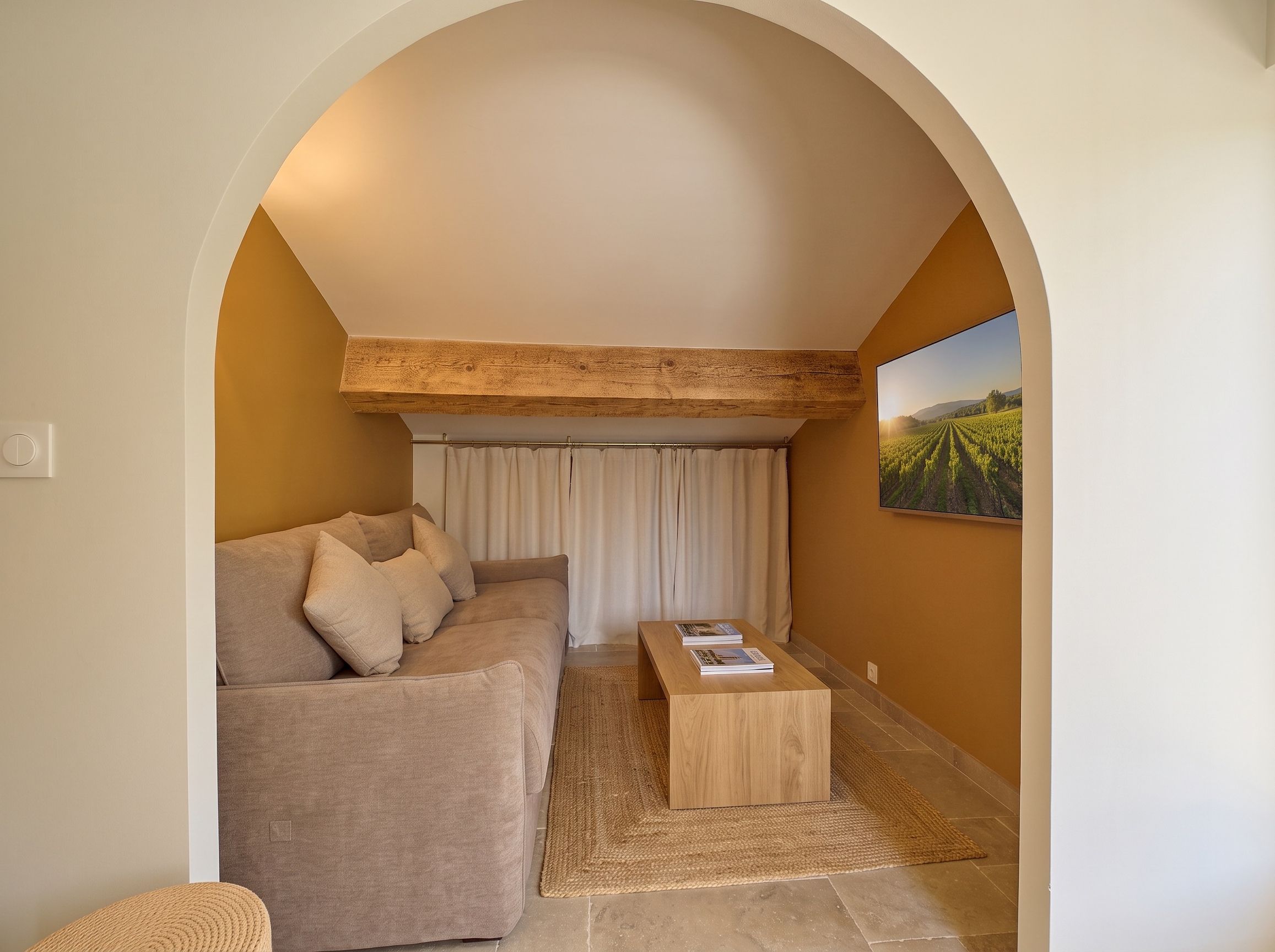 A cozy living room with a sofa, a coffee table, and a painting of a vineyard.