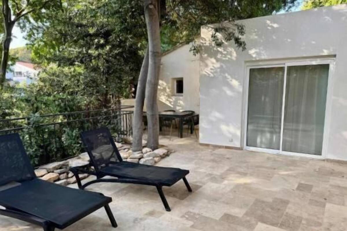 A patio area with two lounge chairs, a table, and a white building with a sliding glass door.
