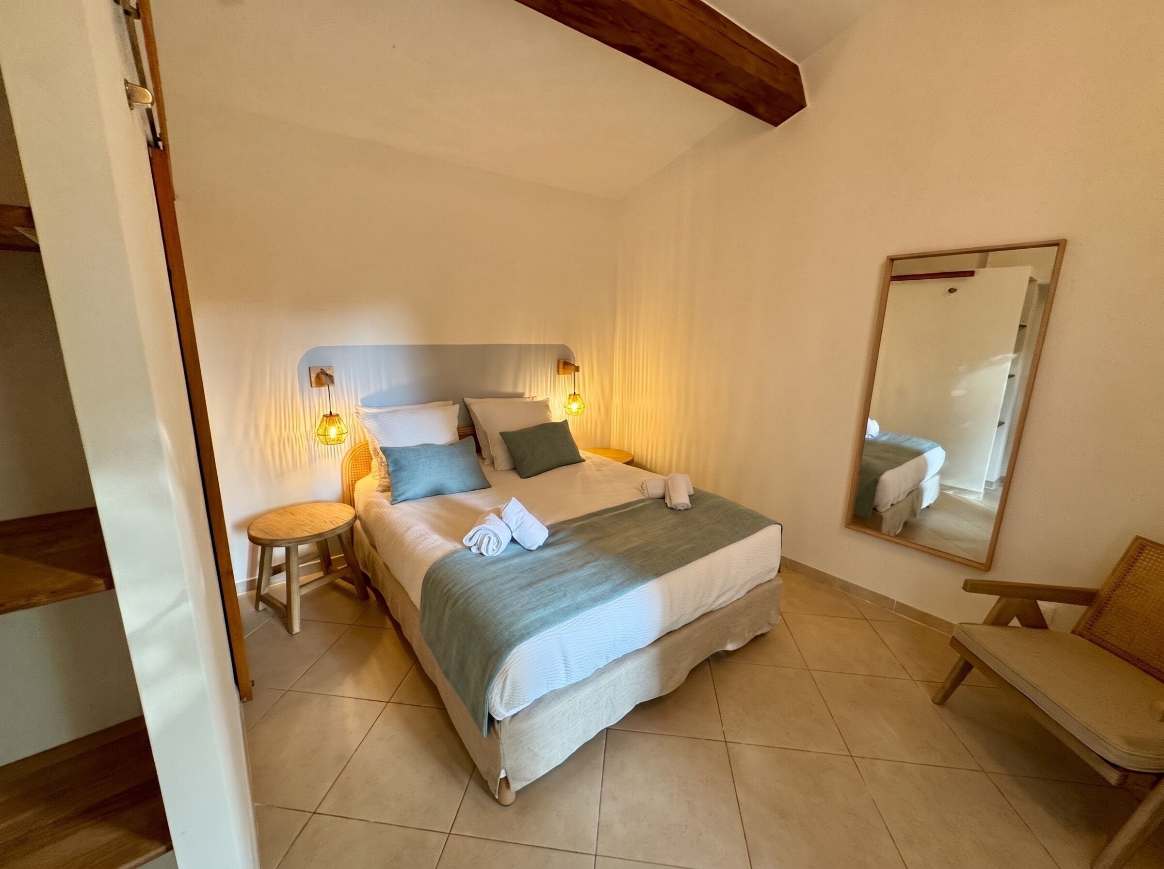Une chambre à coucher comprenant un lit, des tables de chevet, une chaise, un miroir et une poutre en bois au plafond.