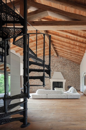 Eine Wendeltreppe, ein Kamin aus Stein und ein Ecksofa in einem Raum mit Holzbalken und einer Steinwand.