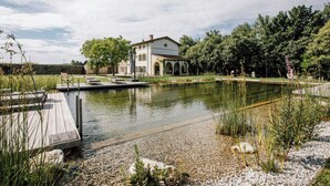 Une maison avec un étang, un quai et de la verdure tout autour.