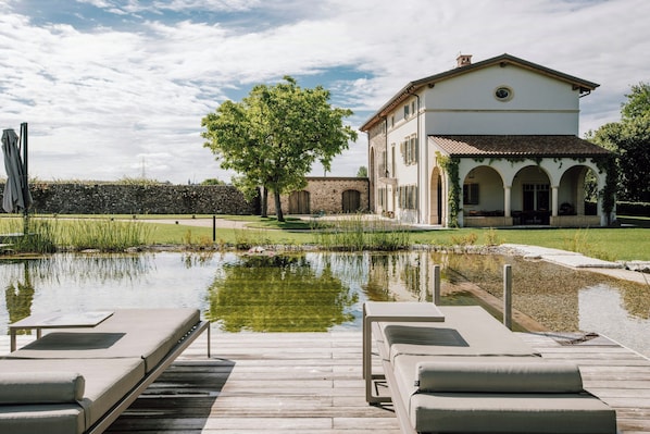 Ein Pool mit Liegestühlen, ein Haus mit Bögen und ein Baum im Hintergrund.