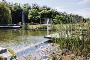 Ein ruhiger Außenbereich mit Teich, einer Holzterrasse und einer Metallskulptur.