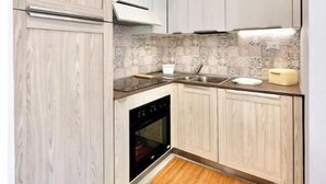 Una cocina moderna con armarios de madera clara, horno integrado, un lavamanos y un salpicadero decorativo.