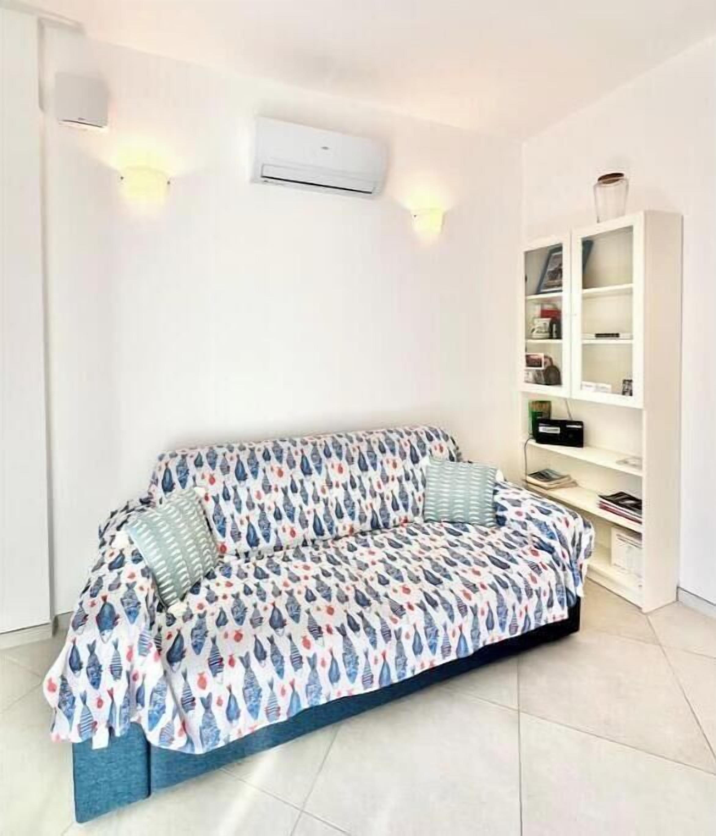 Ein modernes Wohnzimmer mit einem gemusterten Sofa, einer weißen Schrankwand und einer Klimaanlage an der Wand.