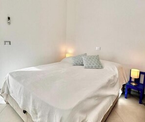 Un dormitorio con cama, almohadas, mesita de noche y lámpara.