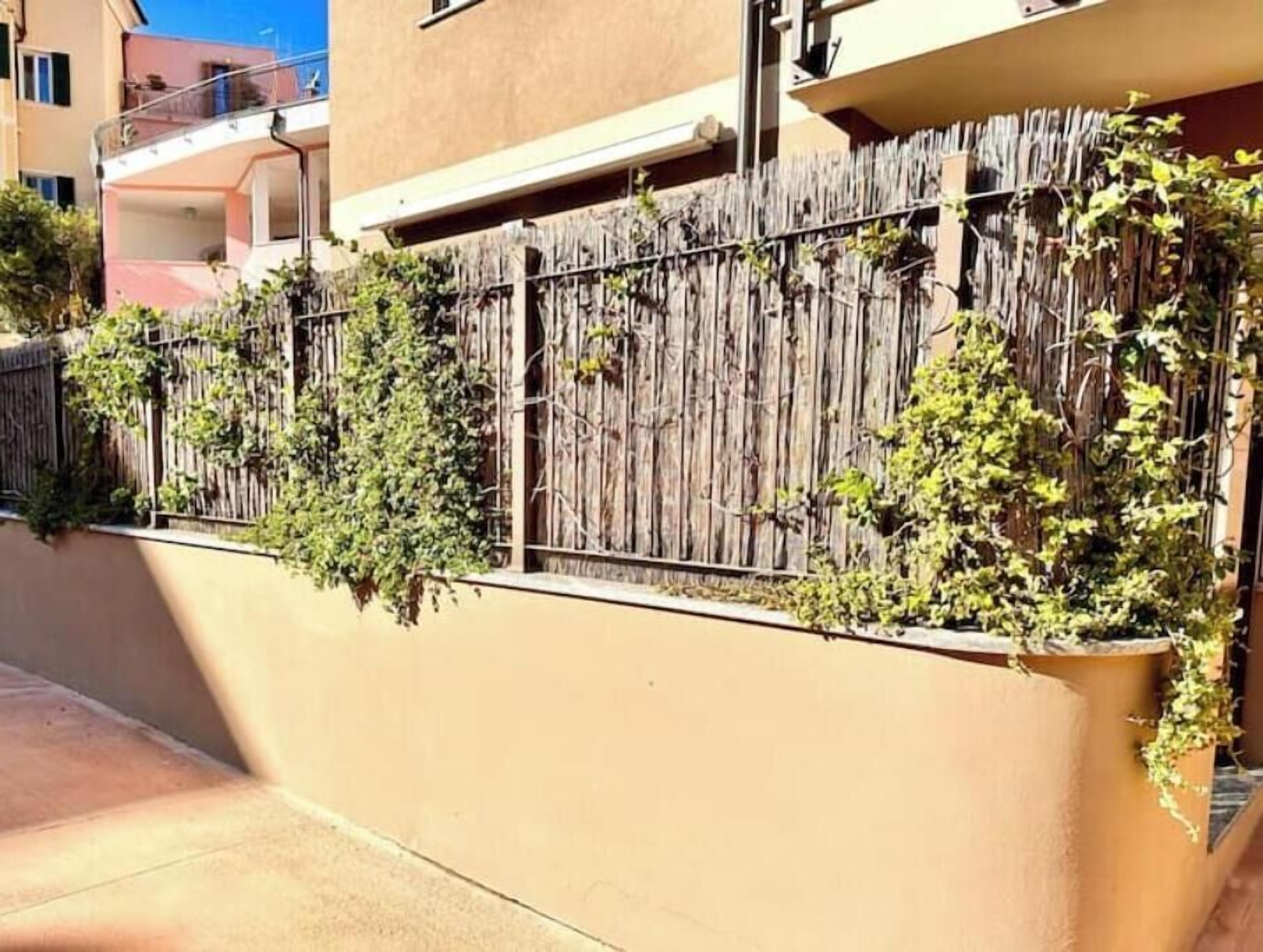 A building with a beige exterior, a wooden fence with climbing plants, and a balcony with a railing.
