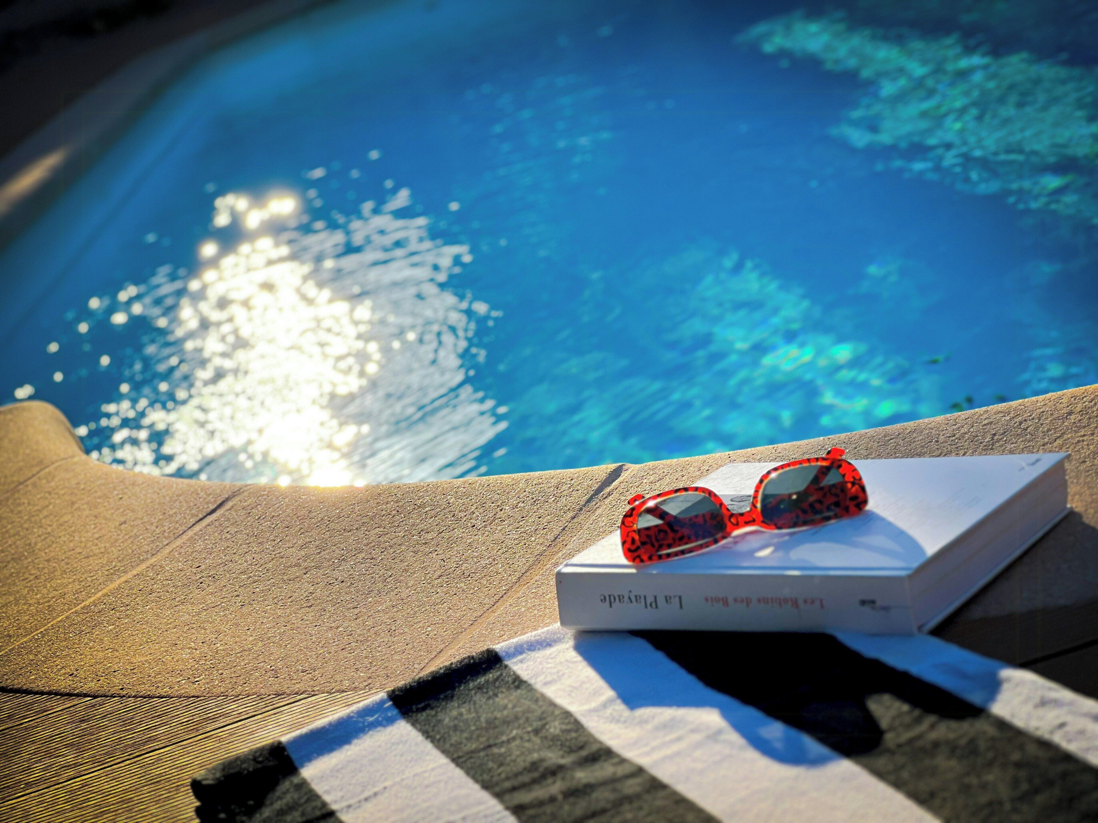 A pair of sunglasses on a book by a poolside.