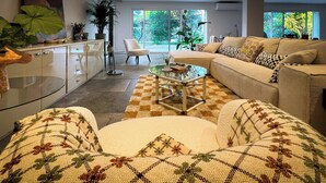 Een moderne woonkamer met een bank, fauteuil, glazen salontafel en een geruit vloerkleed.