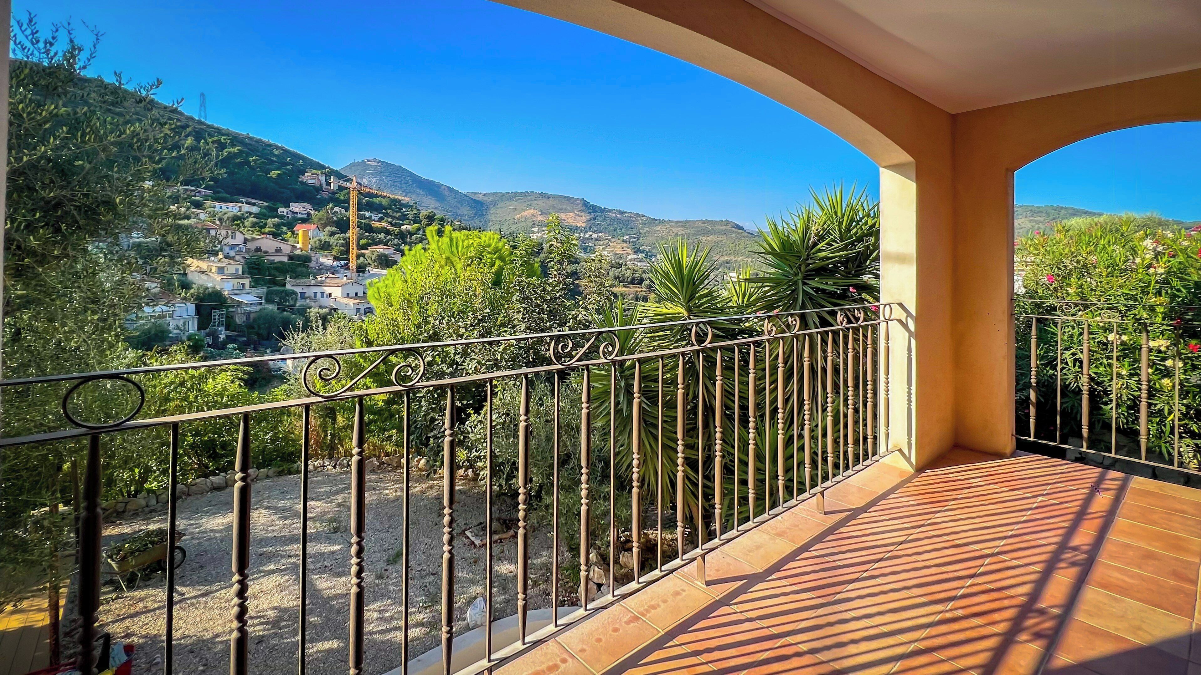 Un balcon donnant sur un village perché sur une colline, avec une rambarde en métal et un sol carrelé.