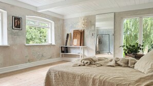 Een slaapkamer met een groot bed, een houten vloer, een raam en een spiegel.