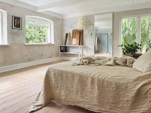 Ein Schlafzimmer mit einem großen Bett, Holzboden, einem Fenster und einem Spiegel.