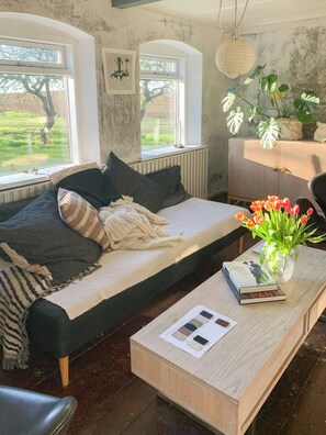 Ein gemütliches Zimmer mit einem Bett, einem Holztisch mit Büchern und einer Vase sowie Blick ins Grüne.