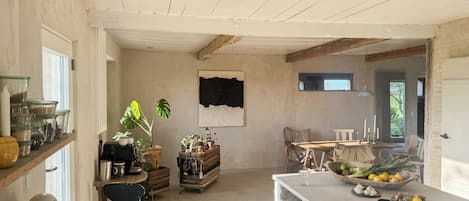 A rustic kitchen with wooden beams, a dining area with a table and chairs, and a window with a view.