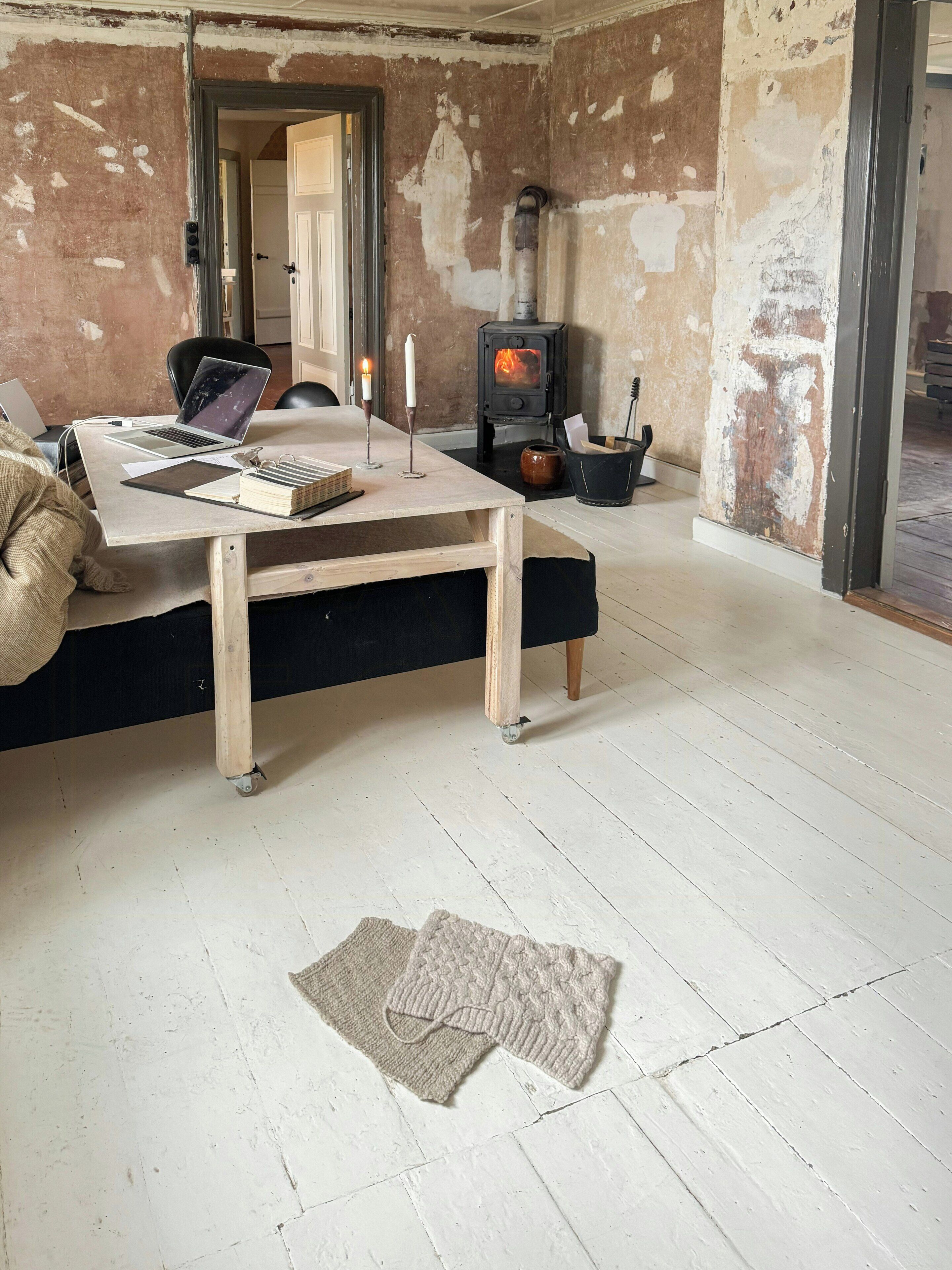 Ein Zimmer mit Holztisch, Laptop, Kerze und Kaminofen.